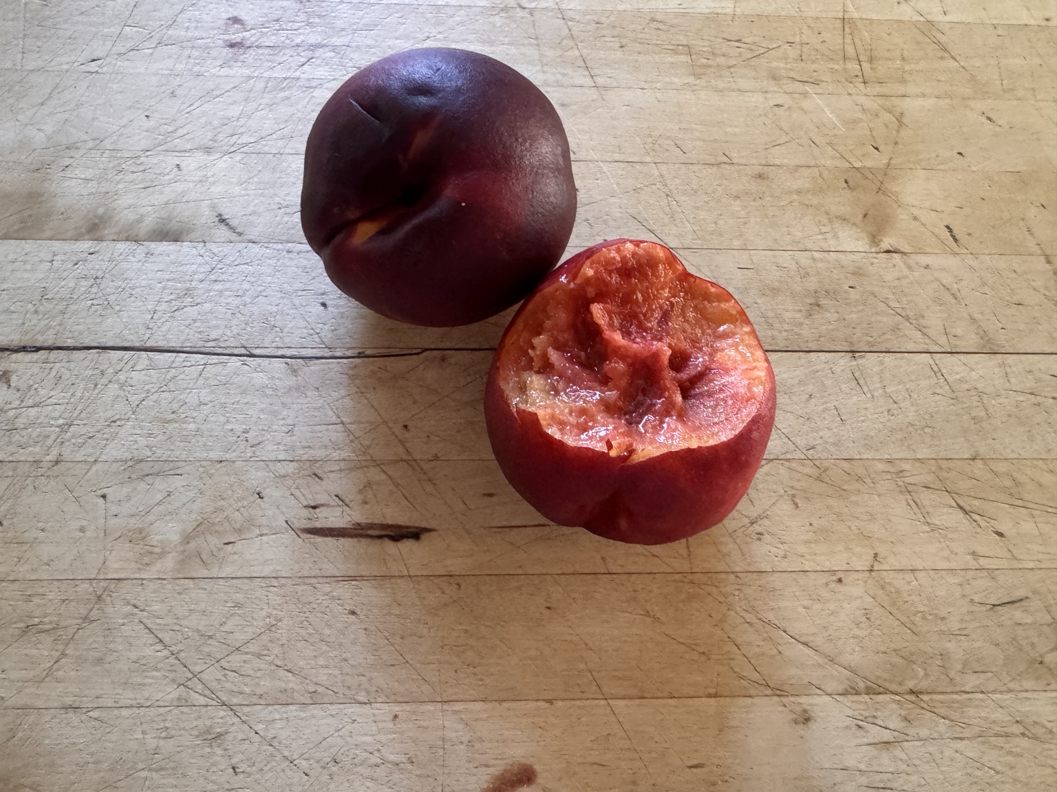 A whole nectarine and a bitten nectarine on a wooden tabletop